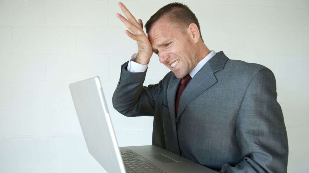 A personal injury lawyer holding a laptop and smacking his head as he is looking at his SEO mistakes