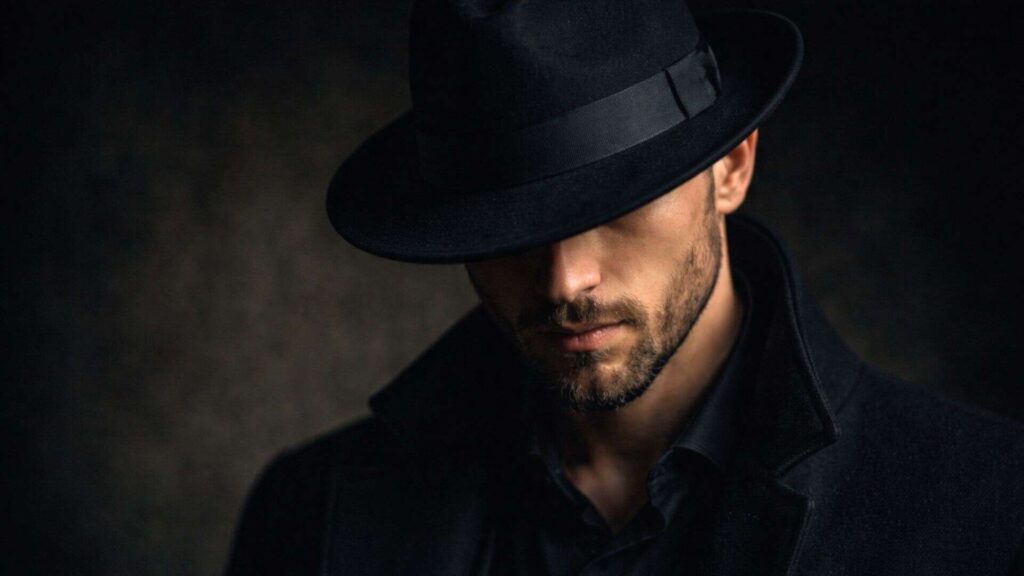 A shady looking character in the shadows with a black hat, signifying black-hat SEO
