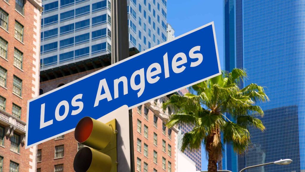 A Los Angeles street sign with LA buildings and palm trees in the background